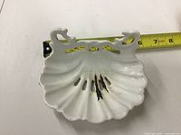 Top view of white enamel shell soap dish showing drainage slots and tape measure indicating 5.5 in. width