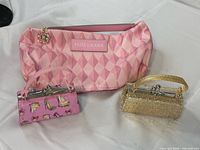 Overview of all three items: Estée Lauder pouch, pink shoe-print mini bag, gold glitter mini bag