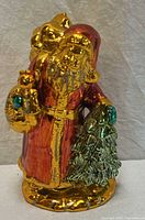Front view of gilded ceramic Santa figurine holding tree and toys
