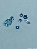 Seven light blue faceted aquamarine stones arranged on flat surface