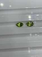 Two lime green oval peridots on white background