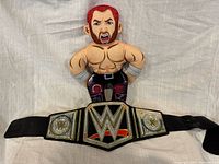 Front view of Kenny Omega plush standing behind WWE belt