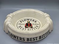 Top perspective of oval cream ceramic ashtray with Flowers Best Bitter logo and four rests