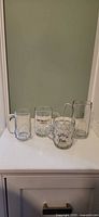 All four glass beer mugs lined up showing fronts and handles