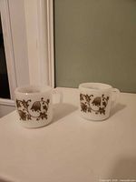 Front view of both milk glass mugs showing floral motif and handles