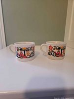 Front view of both Sadler Folk Love mugs showing design and handles