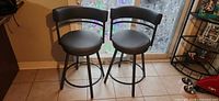 Two dark grey swivel bar stools side by side on tile floor