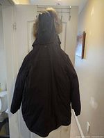 Full back view of black parka hanging, showing hood with faux-fur trim