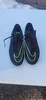 top view of pair of black Nike cleats with neon yellow swoosh