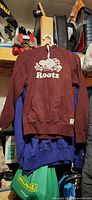 Front view showing burgundy Roots hoodie with logo, pocket and drawstring hood