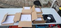 Table with five boxes of white-sleeved vinyl test pressings and one loose record
