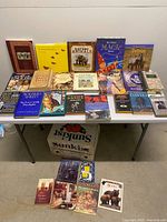 Wide shot of table with ~22 books, Sunkist box beneath, and 9 books on floor
