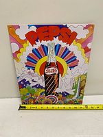 Front view of psychedelic Pepsi metal sign with measuring tape showing approx 12" width