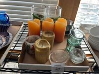 Top view of lot showing orange pillars, gold votives, floral ceramic candle, clear glass cylinders, green-tinted holders