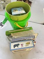 Overall lot showing books stack, activity pad, board book set, nested green buckets with puzzleball inside