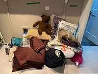 Pile of comforters, pillows, teddy bear, vacuum-sealed quilts and round bag
