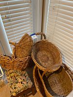 Stack of wicker baskets beside window with floral footstool underneath