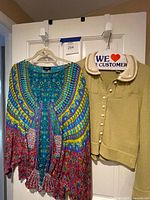 Tolani blouse and green sweater on hangers