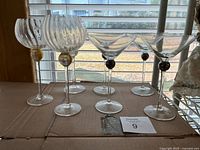 Front view of all six stemware pieces on surface, showing two ribbed globe goblets with gold ball stems and four martini glasses with black ball stems