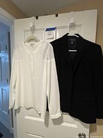 White blouse and black blazer hanging on door