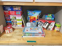 Overall lot showing stacked puzzle boxes, Mega Bloks bag, roll-up piano, activity case and bead jar