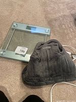 Glass digital bathroom scale and grey Sunbeam heated shawl on carpet