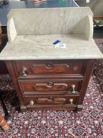 Front view showing marble top, backsplash, three drawers, knob hardware and finish wear