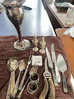 Group shot of entire lot on cloth showing vase, shakers, flatware, knives, server, nutcracker, napkin rings