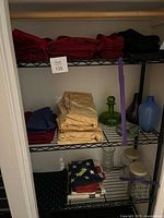 Overall view of closet shelves showing folded red, black, gold, navy, and dark green linens plus American flag