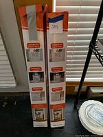 Two unopened tall white boxes with orange header showing retractable mesh gates use scenes