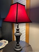 Table lamp illuminated, showing red shade and black metal base