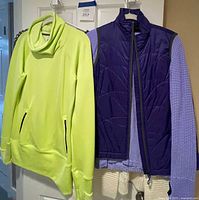 Bright neon yellow-green athletic hoodie and purple quilted vest hanging on a door (other garments visible)