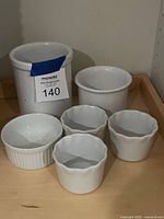 six white ceramic pieces grouped: large crock, medium bowl, ribbed ramekin, three fluted ramekins