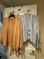 Two cardigans, tan bubble-sleeve and blue cable-knit, with pink sweater and lace dress partially visible