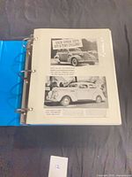open binder with sheet showing two black-and-white vintage car ads