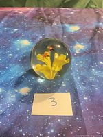 Overall view of spherical glass paperweight with internal yellow flower