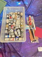 Overview of bin with paint jars, cement tube, brushes and sheets