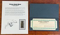 Information sheet and certificate folder displayed side by side; spade coin visible inset on sheet