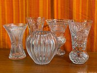 Group shot of five clear cut crystal vases on wood surface