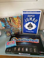 Group shot showing Outsmarted board game, Super Jumbo Playing Cards, 1990s music trivia cards, and jigsaw puzzle