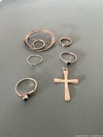 All six sterling silver pieces laid out: circle brooch, four rings and cross pendant