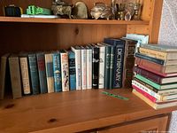 Shelf of upright hardcovers and stack of books on right