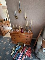 Overview showing dresser, wall sconces, brass and glass holders, bundle of multicolour taper candles on floor