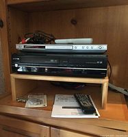 Front view of JVC CD player stacked above Toshiba DVD VCR recorder with remotes and accessories visible