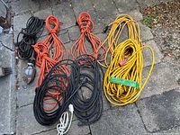 Overall view of five extension cords and utility light coiled on ground