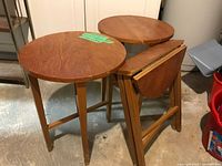 Three round solid wood folding tables, two open one folded