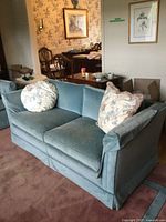 Front view of teal loveseat with two floral pillows
