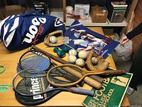 overview of table with rackets, bats, balls, gloves, bag, poster, dumbbells
