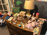 Overview of dresser top showing lamp, ballet shoes, figurines, lunch box and pastel decorations