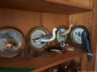 Shelf with brass-rimmed bird plates, wooden shorebirds, duck decoy, flat blue bird, small geometric ornament
